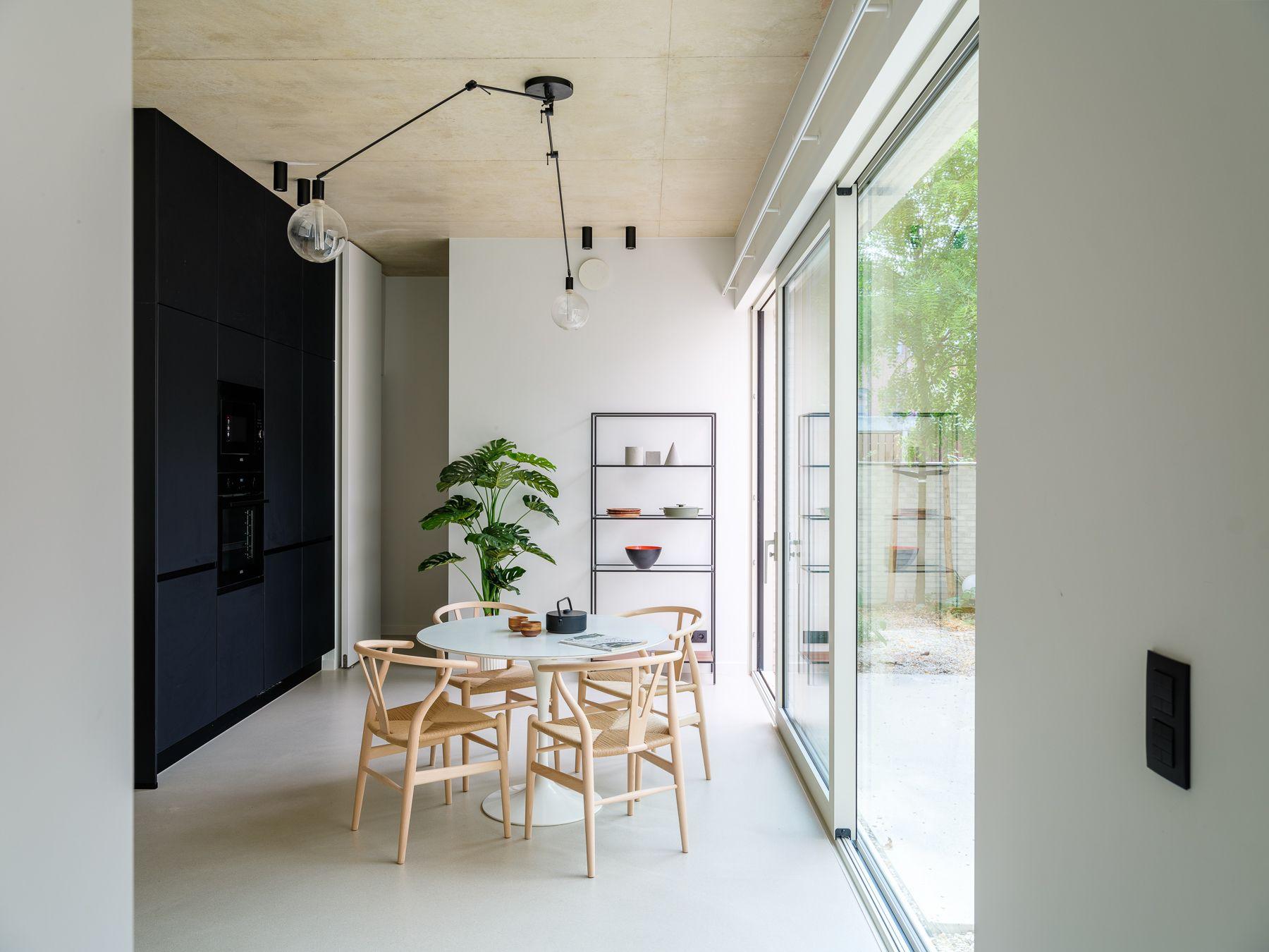 Eethoek met een ronde tafel en houten stoelen naast een zwarte kastenwand en een glazen pui naar buiten, in een woning van het project Nieuwland 28-40 in Gent.