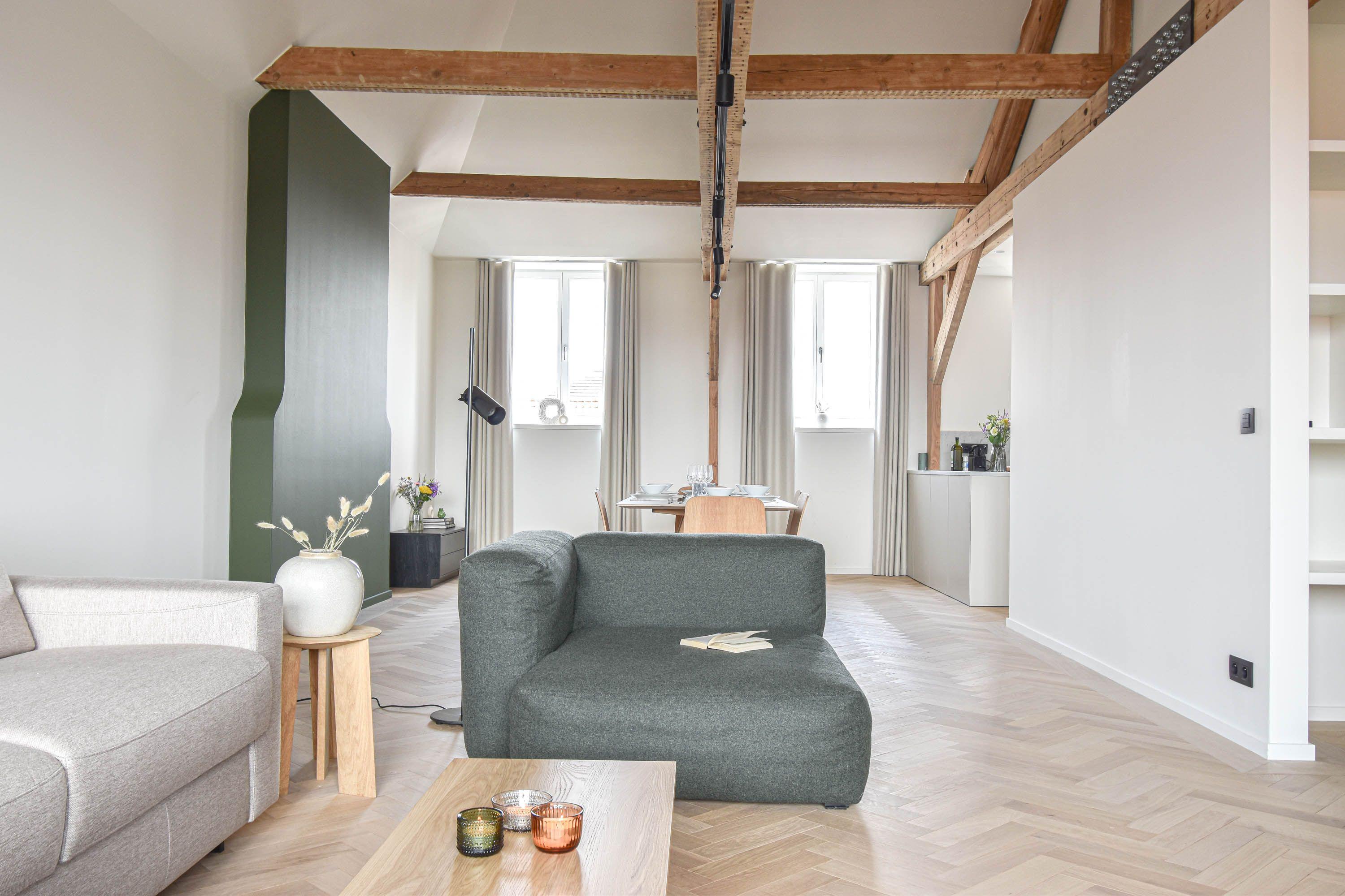 Leefruimte onder houten dakbalken met visgraatparket, in een van de vijf appartementen van het project Belfortstraat 29 – Onderstraat 75A in Gent.